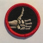 A haunted attraction badge featuring a skeletal hand making a gesture, embroidered with red and blac.
