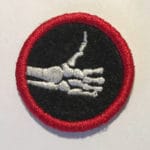 Embroidered badge featuring a skeletal hand with a pointing finger on black background.